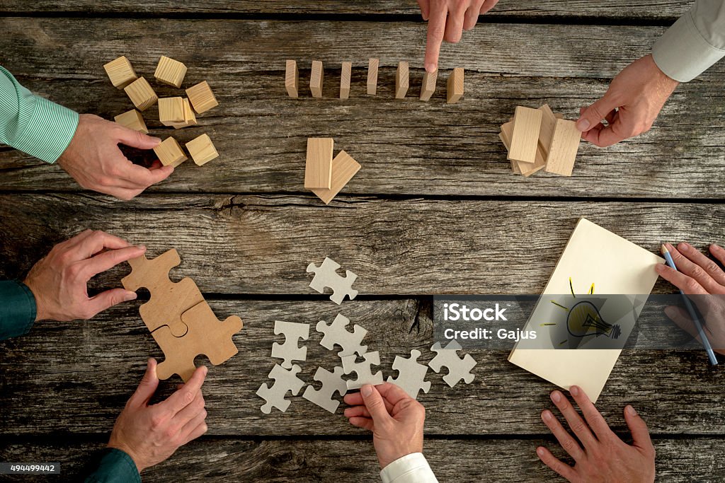 Concept of teamwork, strategy, vision or education Businessmen planning business strategy while holding puzzle pieces, creating ideas with light bulb drawn on paper and rearranging wooden blocks. Conceptual of teamwork, strategy, vision or education. Challenge Stock Photo