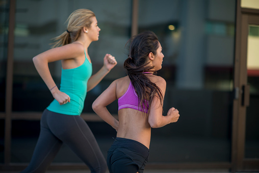 Two girl friends are running together outside and are training together on a sunny day.