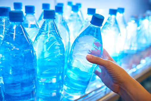 Human hand taking mineral water from shelf in supermarket