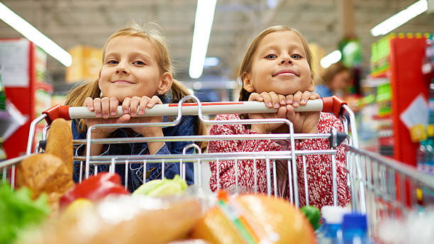 Little sisters doing shopping Portrait of two little girls with shopping cart child pushing grocery cart stock pictures, royalty-free photos & images