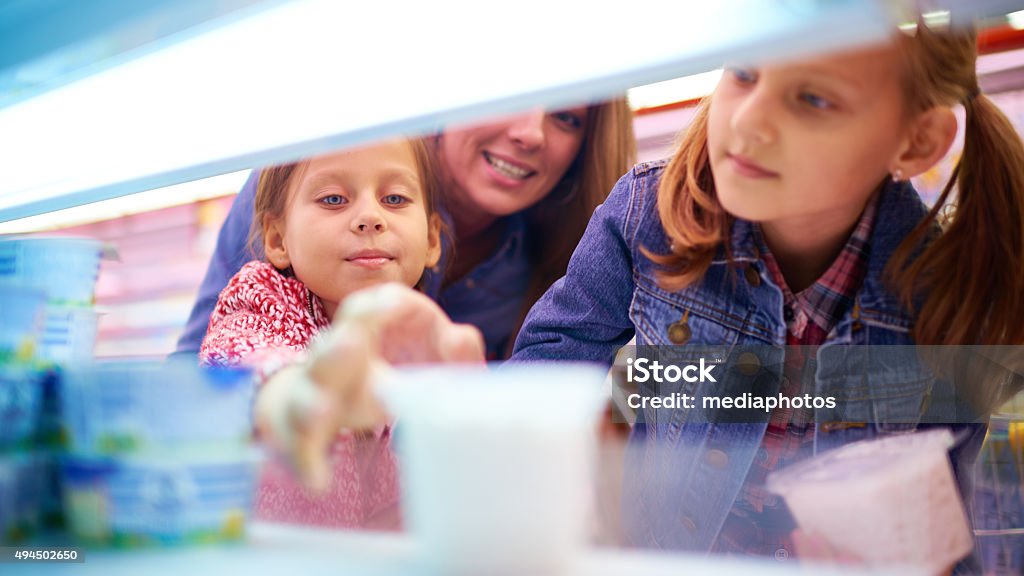 Taking yogurt in supermarket Two little girls and their mom shopping in dairy department Yogurt Stock Photo