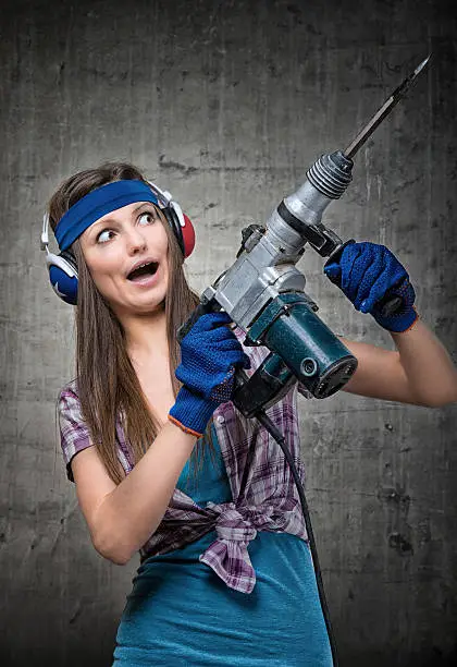 Humorous portrait of a housewife using jackhammer to drill into wall
