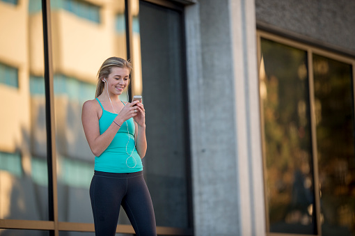 A collge age girl is standing outside in workout clothing and is texting a friend after a run.