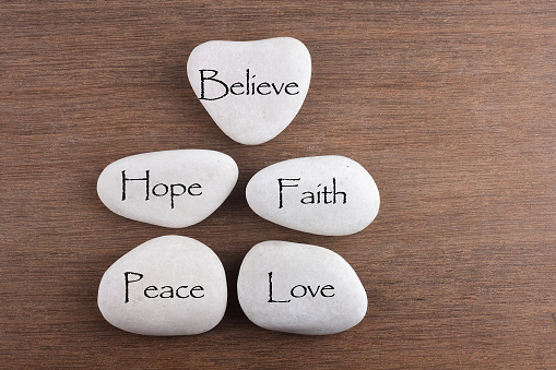 White stones with love, believe, faith, hope, peace word on wooden background