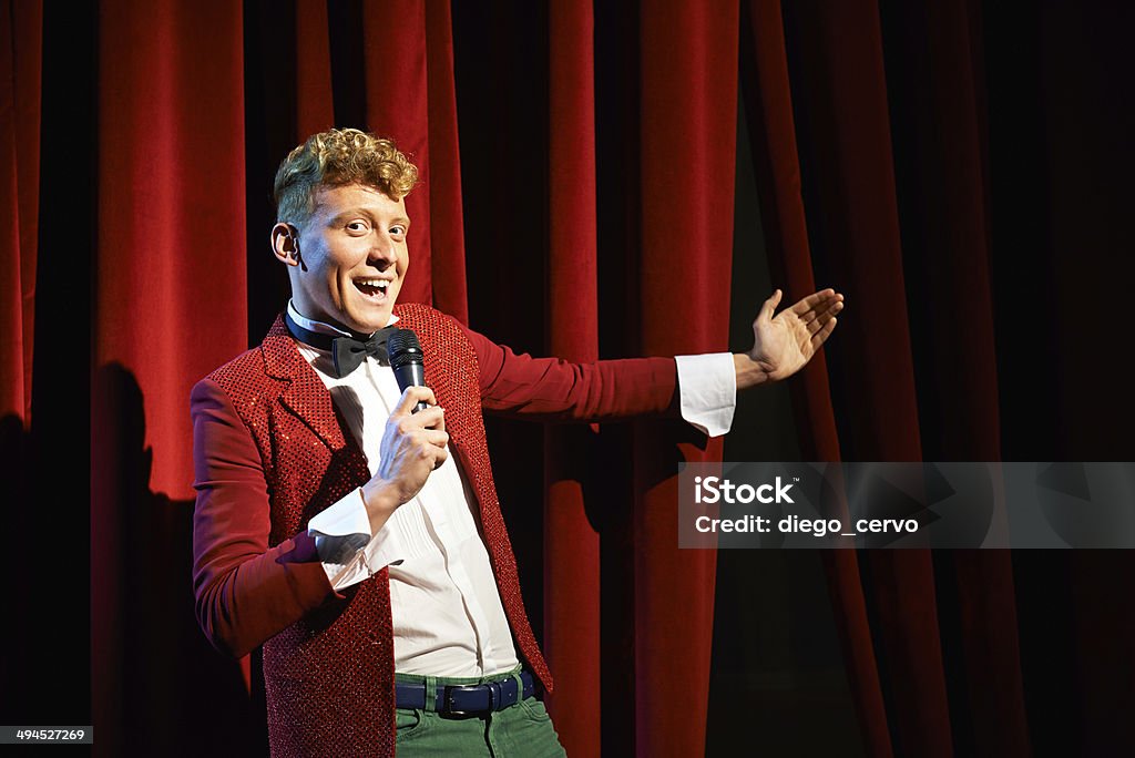 Anchorman talking to spectators and announcing show Arts and entertainment in theatre with funny man working as anchorman, standing against red curtains with microphone Broadway - Manhattan Stock Photo