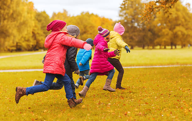 group of happy little kids running outdoors autumn, childhood, leisure and people concept - group of happy little kids playing tag game and running in park outdoors playing tag stock pictures, royalty-free photos & images