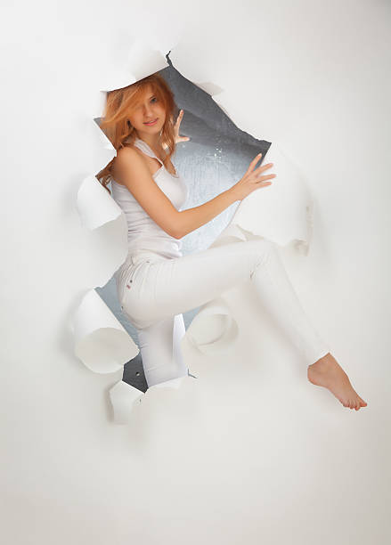 Beautiful red-haired girl in white trousers in a hole in the paper.
