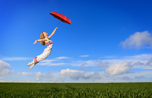 Beautiful young woman flying on a green meadow with a red umbrella