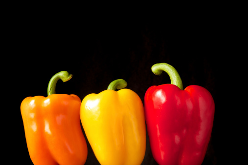 Three colourful peppers in front of a black background.