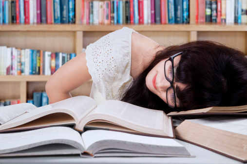 Tired student girl with glasses sleeping on the books in the library