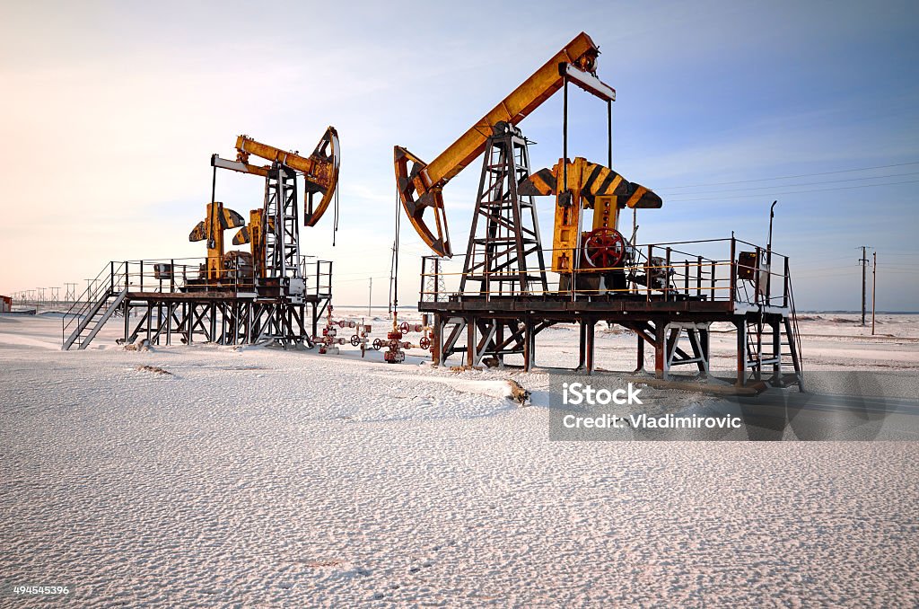 Oil rig back light Oil pump cold winter and snow. Back light, white cloudy and blue sky background, sunlight Crude Oil Stock Photo