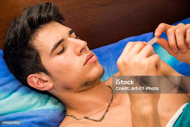 Young Man In Bed Measuring Fever With Thermometer Stock Photo - Download Image Now - 2015, Adult, Adults Only