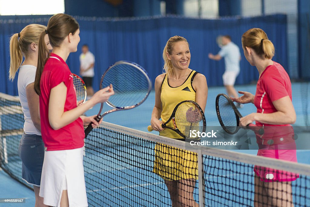 Female Indoor Tennis Players Group of four women talking by the tennis net after playing a doubles match.    Tennis Stock Photo