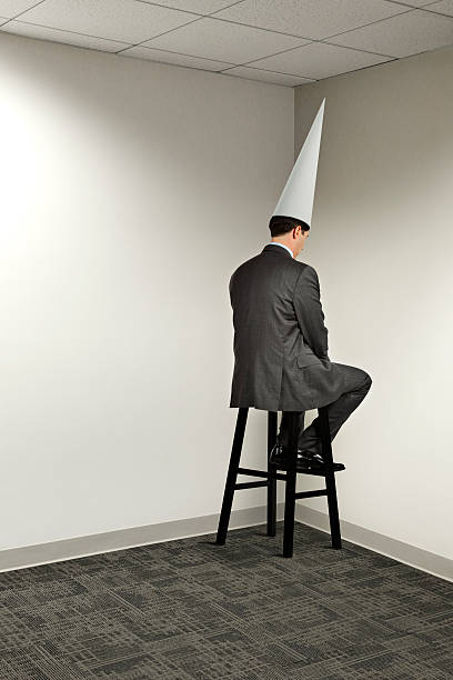 Businessman Sitting In Office Corner Wearing Dunce Cap Stock Photo -  Download Image Now - iStock