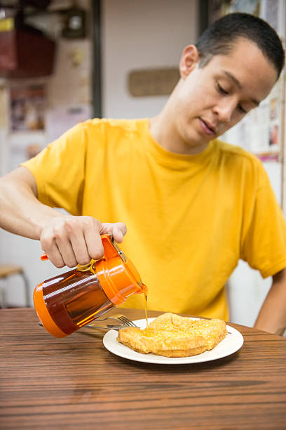 Pan Asian Man Pouring Syrup over French Toast Young man pouring syrup over Hong Kong style French toast, consisting of 2 pieces of bread filled with coconut jam.  Typical breakfast in Hong Kong. chinese ethnicity china restaurant eating stock pictures, royalty-free photos & images