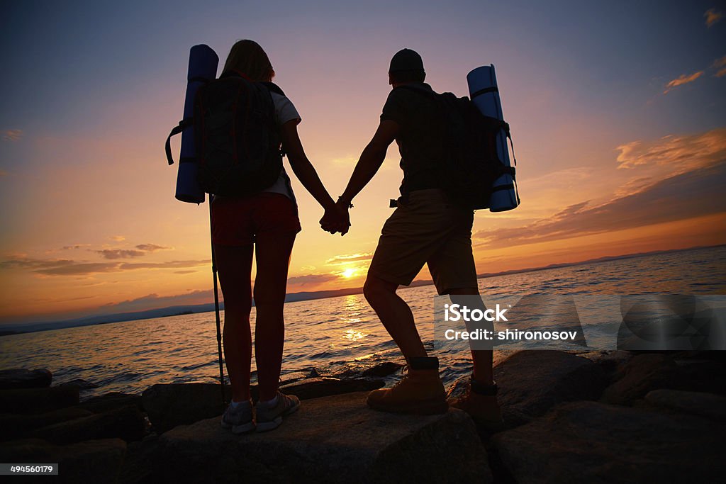 Hikers at sunset Image of beautiful scene of sunset and backs of couple of hikers enjoying it Adult Stock Photo