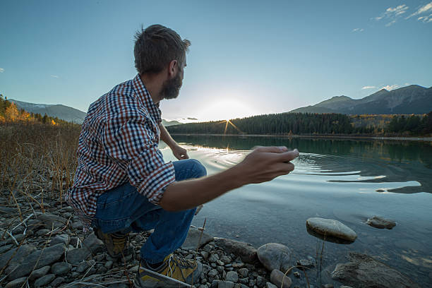 giovane uomo di lago al tramonto far saltare i sassi sull'acqua - throwing people stone tossing foto e immagini stock