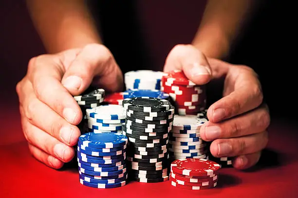 Photo of Man's hands move the winnings casino chips on red table.