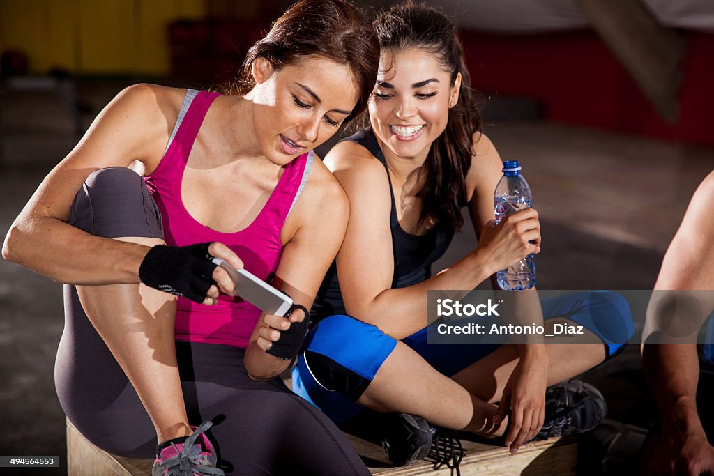 Social networking at a gym Cute female friends texting and social networking at a gym gym Cross Training Stock Photo