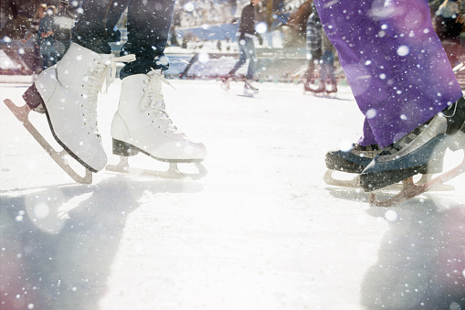 Closeup skating shoes ice skating outdoor at ice rink. Magical glitter of snowy snowflakes and bokeh. Healthy lifestyle and winter sport concept at sports stadium.