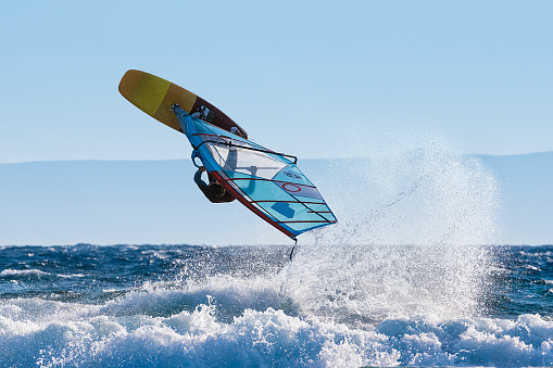 Windsurfing in sea with splashing water. Perspective from behind on sail towards the surfer.