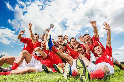 Cheerful soccer team sitting and holding winning trophy.  