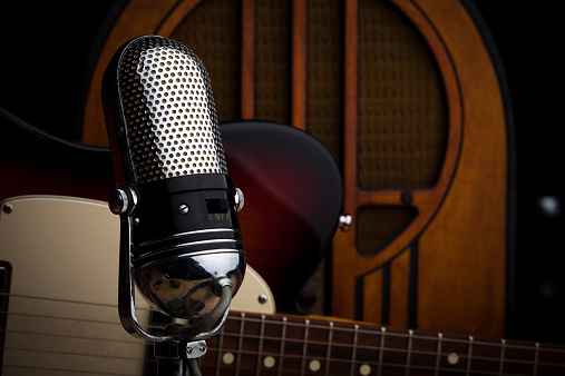 Still life shot of a classic microphone, an electric guitar, and a vintage radio.