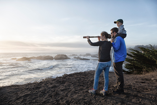 Family with spyglass looking toward ocean at sunset. Concept for discovery or looking toward future.