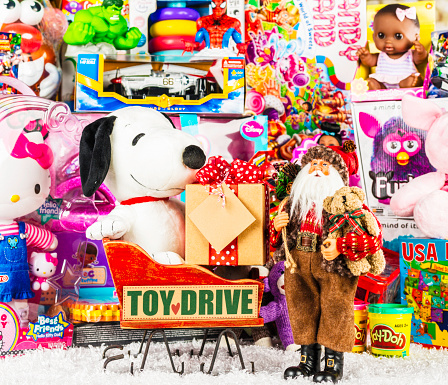 Suffolk, Virginia, USA - December 4, 2013: A horizontal studio shot of a large collection of American brand toys with a Santa figurine at the front. Next to Santa is a wooden sleigh with a plush Snoopy toy in it. Snoopy is holding a gift box.