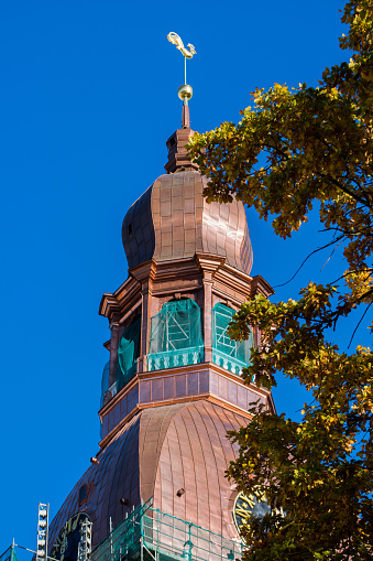 The Rigas Dome, or Riga Cathedral has been under rennovation for a year and now one can see the copper as it once was when the dome was built in 1727. Also in the image is some of the scaffolding, the brass rooser and a yellow leafed tree.