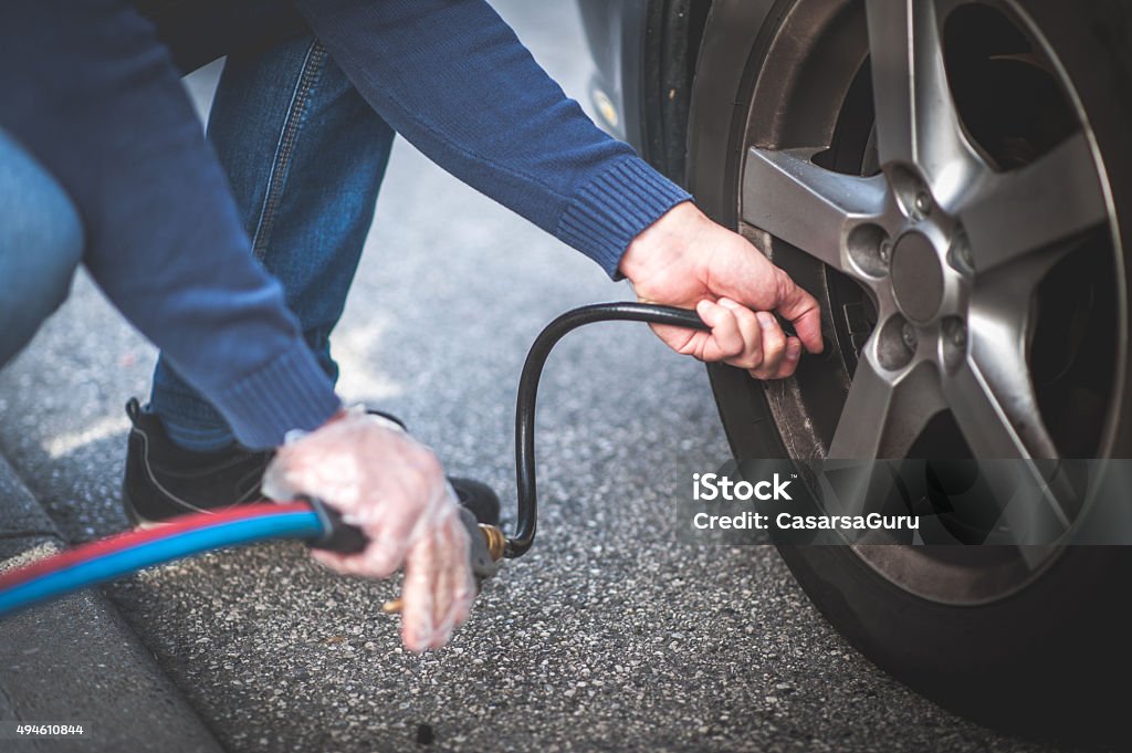 Man Checking Pressure and Inflating Car Tire Man checking pressure and inflating car tire Tire - Vehicle Part Stock Photo