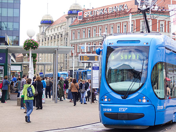 Zagreb, Сroacia - September 22, 2014: Streetcar station in the Zagreb central square Ban Jelacic. A blue Tram is just living the station, while a lot of people wait at station for next tram. In background are houses with lot of commercial panels. It is grey autumn day.