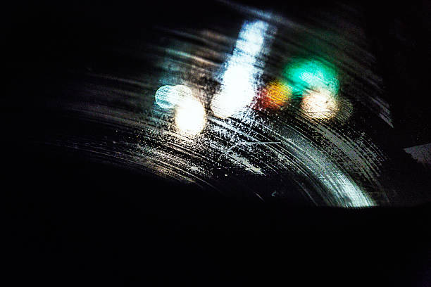 POV night shot of intentionally out of focus windshield wiper streaked abstract vehicle headlights and tail lights looking through the rainy, sloppy, opaque windshield of a speeding car.