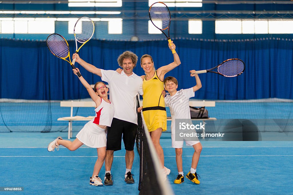 Cheerful Family Playing Indoor Tennis Portrait of a happy young family posing by the tennis net in the indoor tennis court.   Daughter Stock Photo