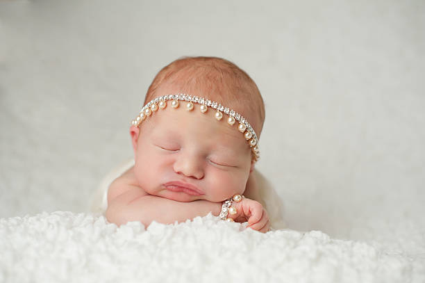 Newborn Baby Girl with Rhinestone and Pearl Headband Portrait of a red headed, 2 week old, newborn baby girl. She is wearing a rhinestone and pearl headband and bracelet and is sleeping on a white, gauzy blanket. baby bracelet stock pictures, royalty-free photos & images