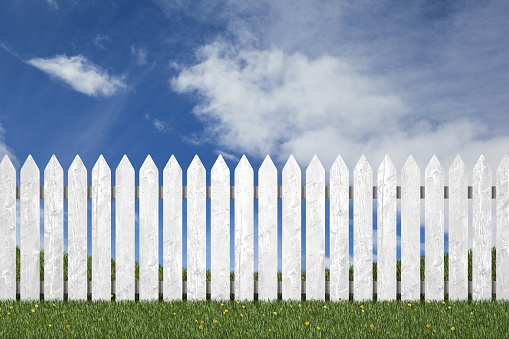 Picket fence with green grass and blue sky in the background.