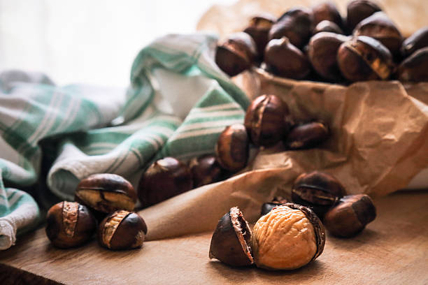 Preparation of healthy autumn snack.Fresh roasted chestnuts on wooden cutting board with paper sack full of chestnuts in blurred background.