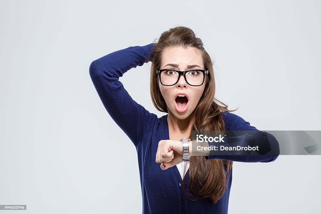 Woman holding hand with wrist watch and looking at camera Portrait of shocked young woman holding hand with wrist watch and looking at camera isolated on a white background Urgency Stock Photo