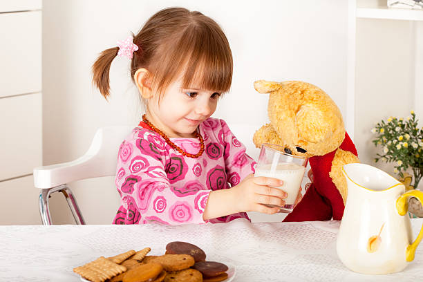 Girl gives glass of milk to teddy bear stock photo