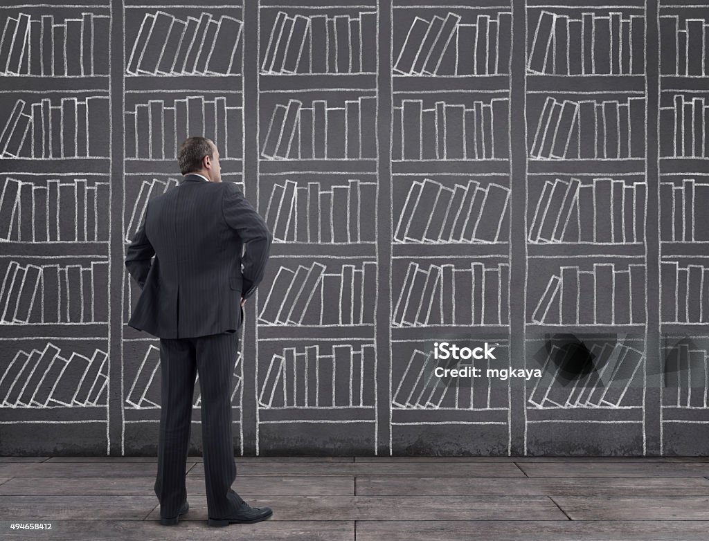 Businessman with Bookshelf Sketched on the Wall Rear view of businessman standing on wooden floor with bookshelf sketched (chalk drawing) on the wall. Shelf Stock Photo