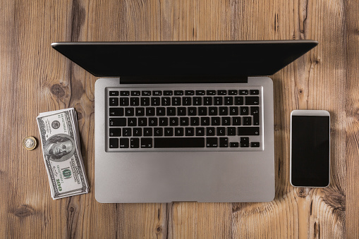 Business folder with dollar bills, opened the laptop and smartphone on wooden table surface.