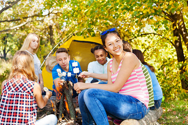istock Happy teens hold marshmallow sitting on campsite 494662820
