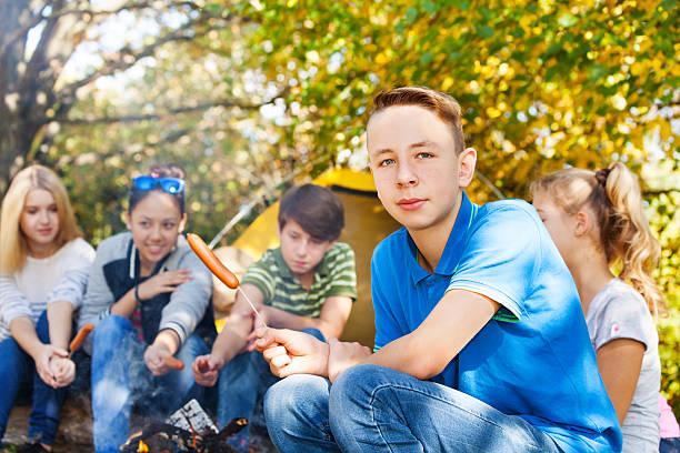 istock Boy and teens sit on campsite with sausages 494663300