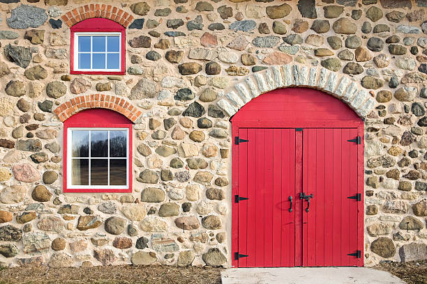 Bright red arched door and two paned windows set in an old field stone wall.  Lots of texture, color, and craftsmanship.