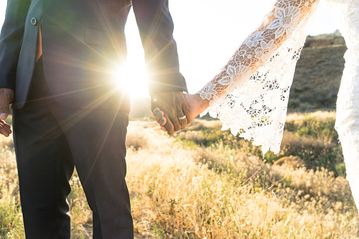 An Interracial couple holding hands backlit by the flaring sun