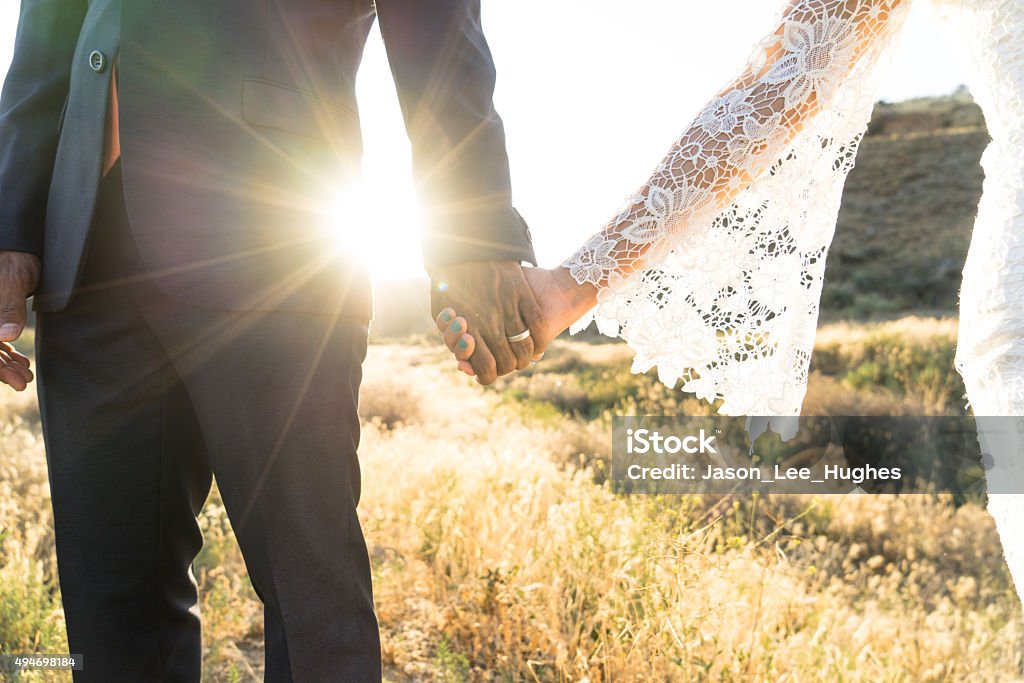 Interracial couple holding hands at wedding An Interracial couple holding hands backlit by the flaring sun Wedding Stock Photo