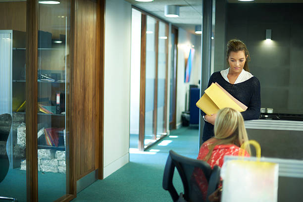 two young female office workers chatting young female office worker or work experience student , sitting at her desk and chatting to her colleague. school receptionist stock pictures, royalty-free photos & images