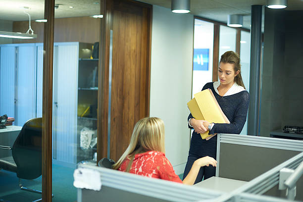 two young female office workers chatting young female office worker or work experience student , sitting at her desk and chatting to her colleague. school receptionist stock pictures, royalty-free photos & images
