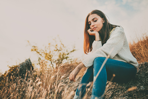 Teenage girl sitting alone on autumn cold day. Lonely sad young woman wearing warm sweater thinking and hesitating. Loneliness and solitude concept.