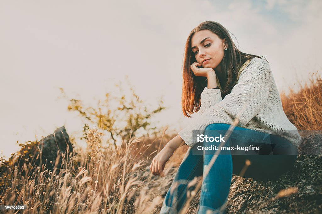 Sad girl thinking outdoors Teenage girl sitting alone on autumn cold day. Lonely sad young woman wearing warm sweater thinking and hesitating. Loneliness and solitude concept. Women Stock Photo